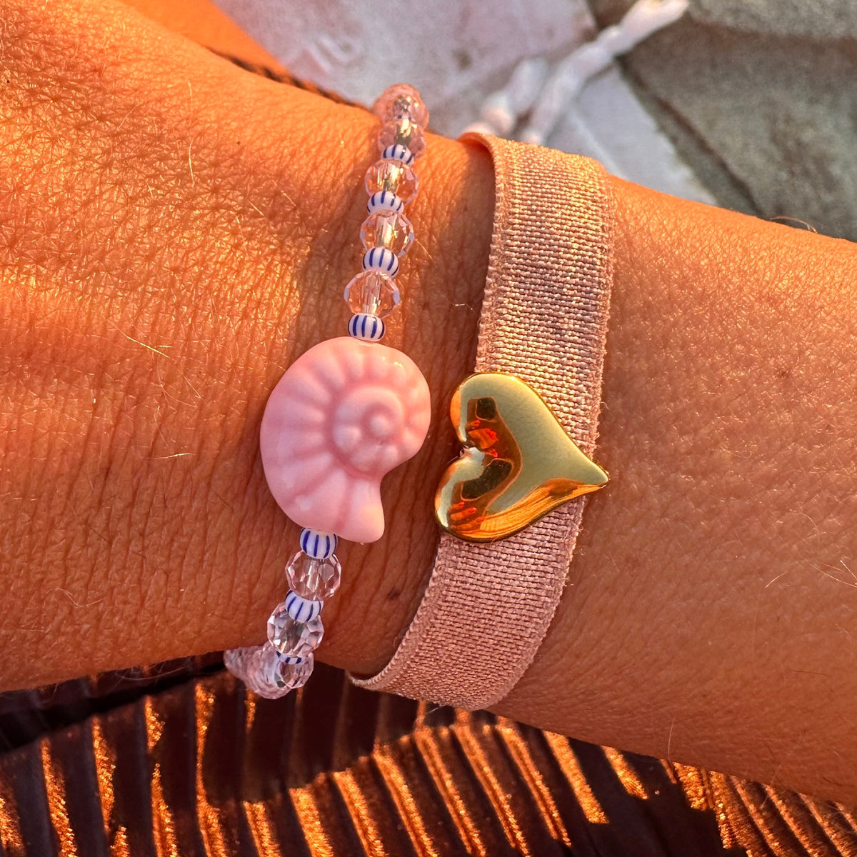 Bracelet perles avec coquillage rose et breloque coeur doree, porte au poignet