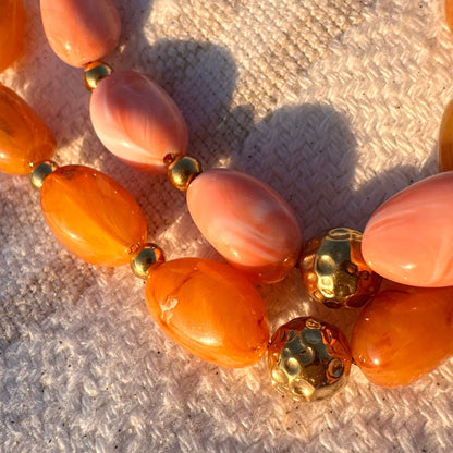 Gros plan des perles en resine orange et de la perle doree marteloe du collier