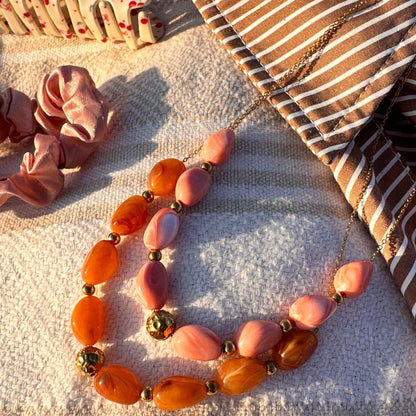 Collier de perles en resine orange et rose pose sur un tissu raye