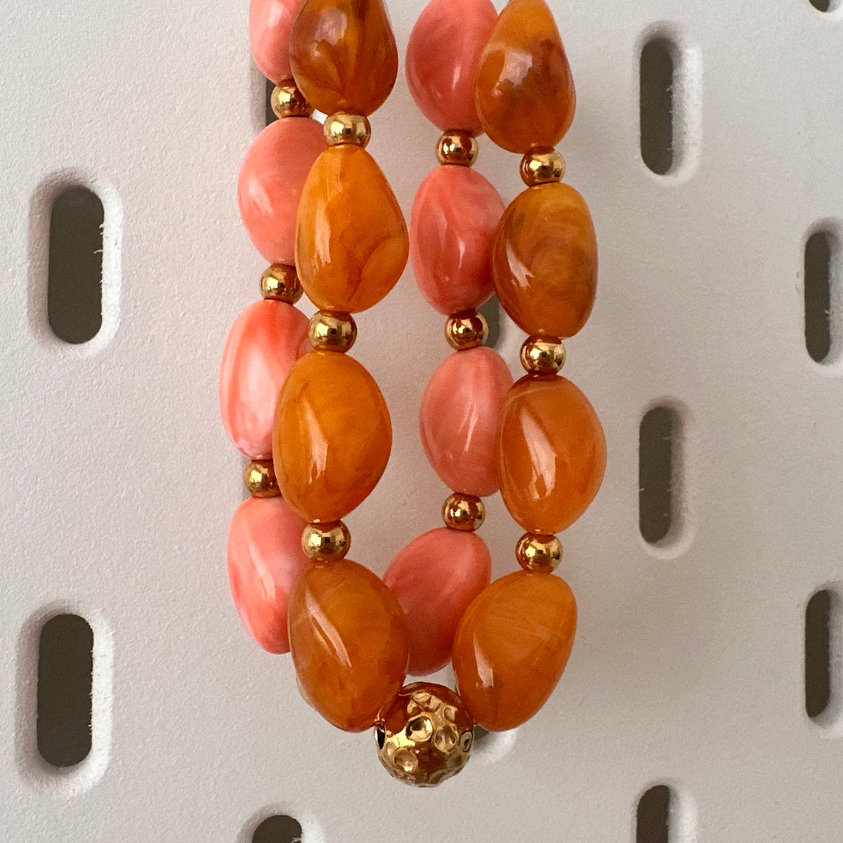 Collier en perles de resine orange et rose presente sur un support bijoux