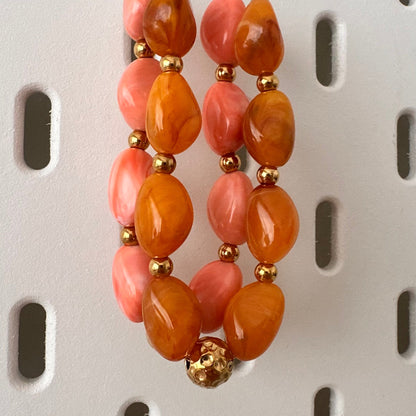 Collier en perles de resine orange et rose presente sur un support bijoux